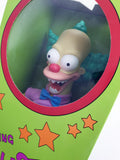 A close-up of a toy figurine resembling a cartoon clown character with a beige head, large white eyes, a pink nose, blue hair, and a purple shirt with a blue bow tie, displayed inside a green box with a circular cutout.
בובה ענקית מדברת בגודל "16 (40 ס"מ) של קראסטי הליצן מהסדרה משפחת סימפסון
יוצרה ע"י ג'אקס פסיפיק בשנת 2024, חדשה באריזה במצב
עשויה ויניל ובד. יש לה שרוך בגב ובורר מצבים (טוב / רע) ובהתאם לבחירה אומר משפטים מהסדרה
דמות פעולה אקשן פיגר בובה צעצוע אספנות איסוף וינטג' וינטאג' מחיר מבצע הסימפסונים